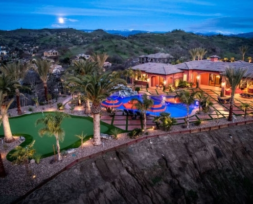 A large home with a pool and a golf course illuminated at night, creating a serene and luxurious atmosphere.
